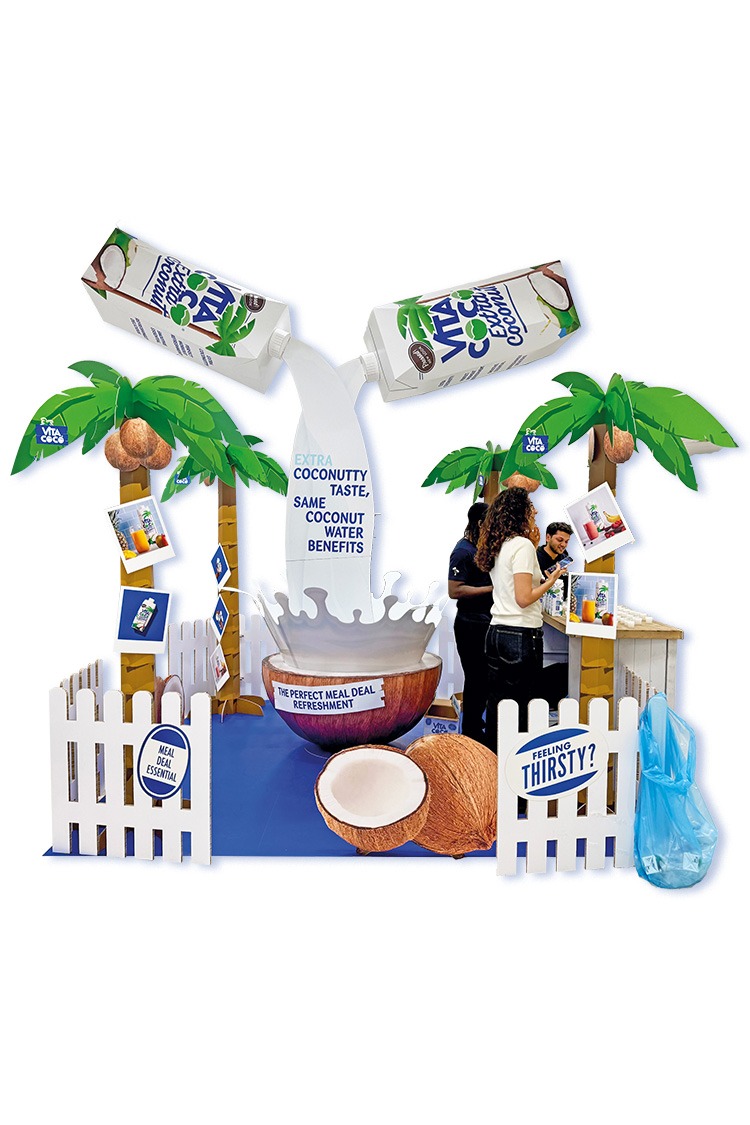 A 3m x 3m space containg large carboard replicas of products and palm trees with a very large half coconut taking centre stage.